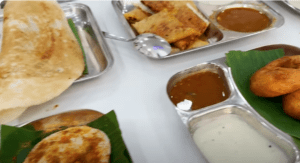 An assortment of South Indian dishes at Udupi Kitchen, including Podi Idli with coconut chutney, Ghee Masala Dosa, Mysore Masala Dosa, Vada with sambhar, and Sheera.